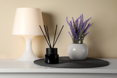 Photo of Aromatic reed air freshener, lamp and lavender flowers on white table indoors