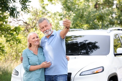 Happy senior couple taking selfie near car outdoors