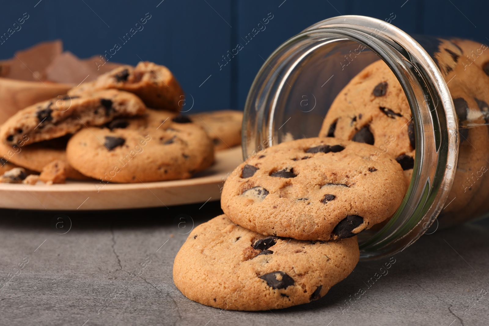 Photo of Glass jar with delicious chocolate chip cookies on grey table, closeup