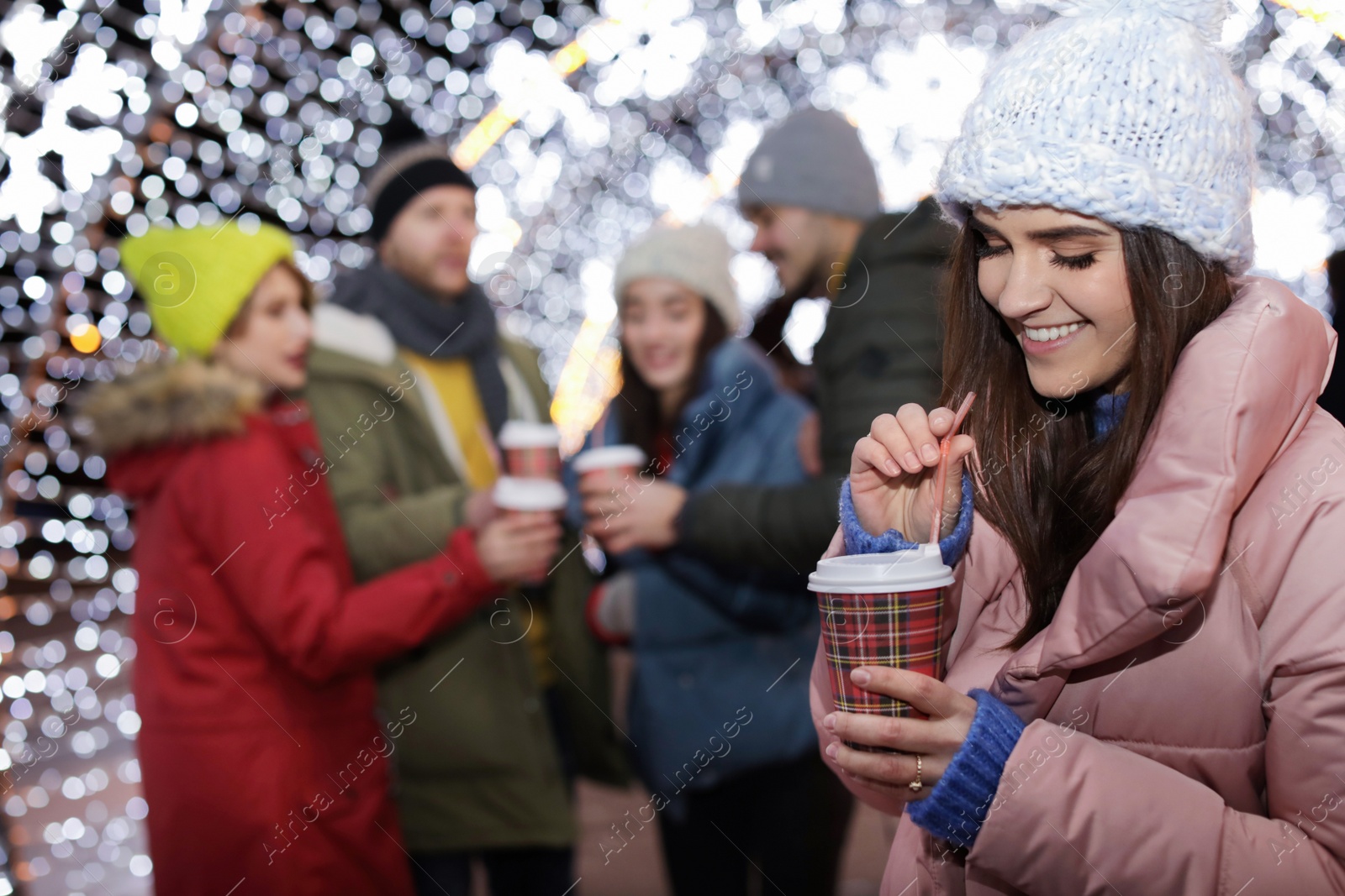 Photo of Happy woman with cup of mulled wine and friends at winter fair. Space for text