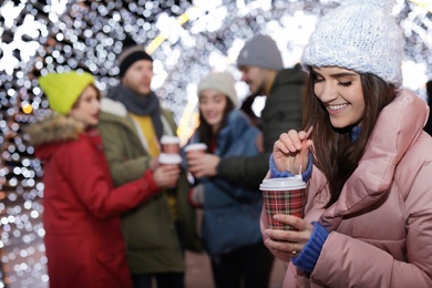 Photo of Happy woman with cup of mulled wine and friends at winter fair. Space for text