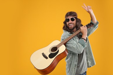 Photo of Stylish hippie man with guitar showing V-sign on orange background, space for text