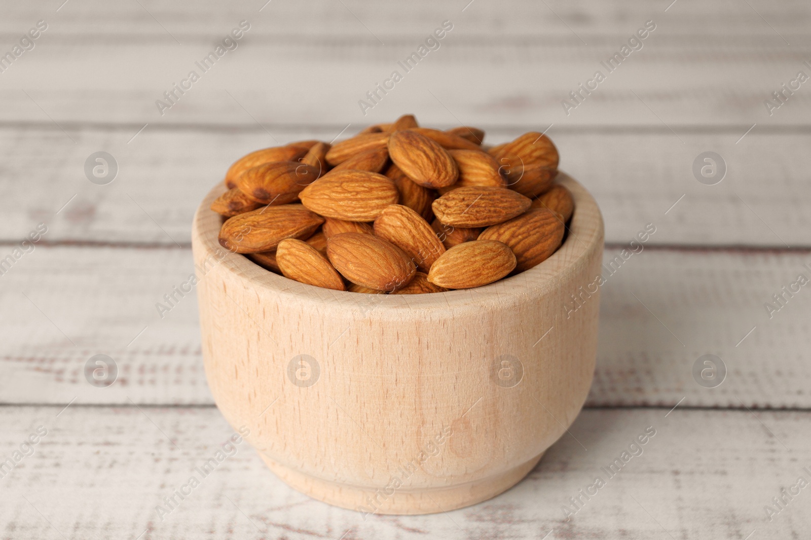 Photo of Tasty almonds in bowl on white wooden table