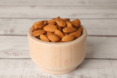 Tasty almonds in bowl on white wooden table