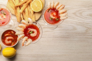 Photo of Tasty shrimp cocktail with sauce in glasses and lemon on light wooden table, flat lay. Space for text
