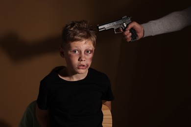 Kidnapper pointing gun at little boy taken hostage on dark background
