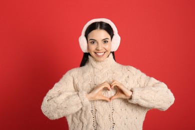 Photo of Beautiful young woman wearing earmuffs on red background