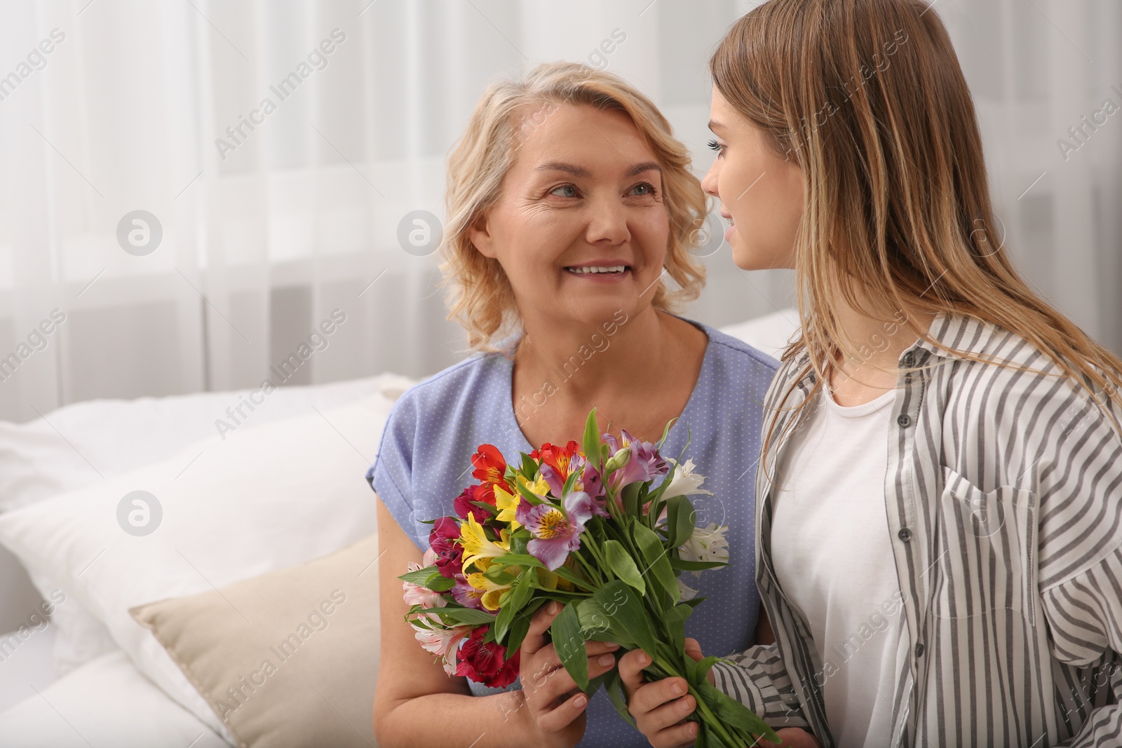 Photo of Young daughter congratulating her mom with flowers at home. Happy Mother's Day