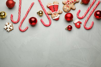 Tasty candy canes, gingerbread cookies and Christmas balls on grey table, flat lay. Space for text