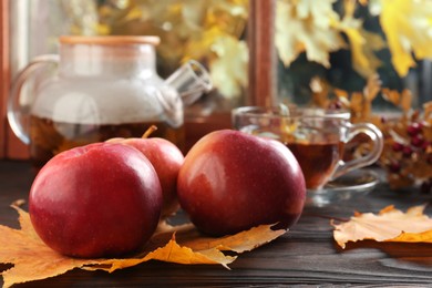 Photo of Apples, hot tea and dry leaves on wooden windowsill, closeup. Autumn atmosphere