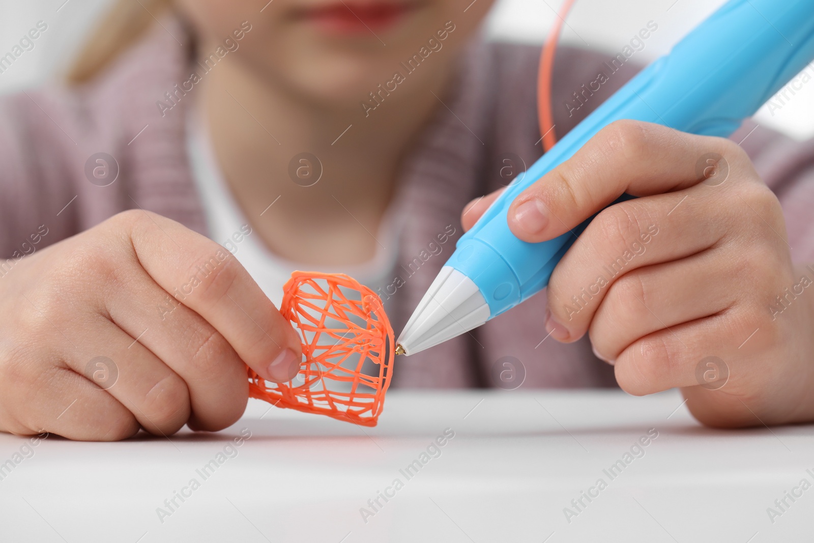 Photo of Girl drawing with stylish 3D pen at white table indoors, closeup