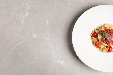 Photo of Tasty pasta with tomatoes, cheese and basil on light grey marble table, top view. Space for text