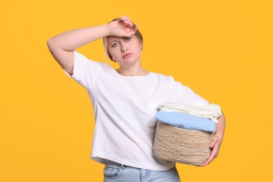 Photo of Tired woman with basket full of laundry on orange background