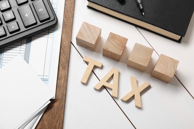 Word Tax made of letters, cubes, calculator, notebook and documents on white wooden table, flat lay