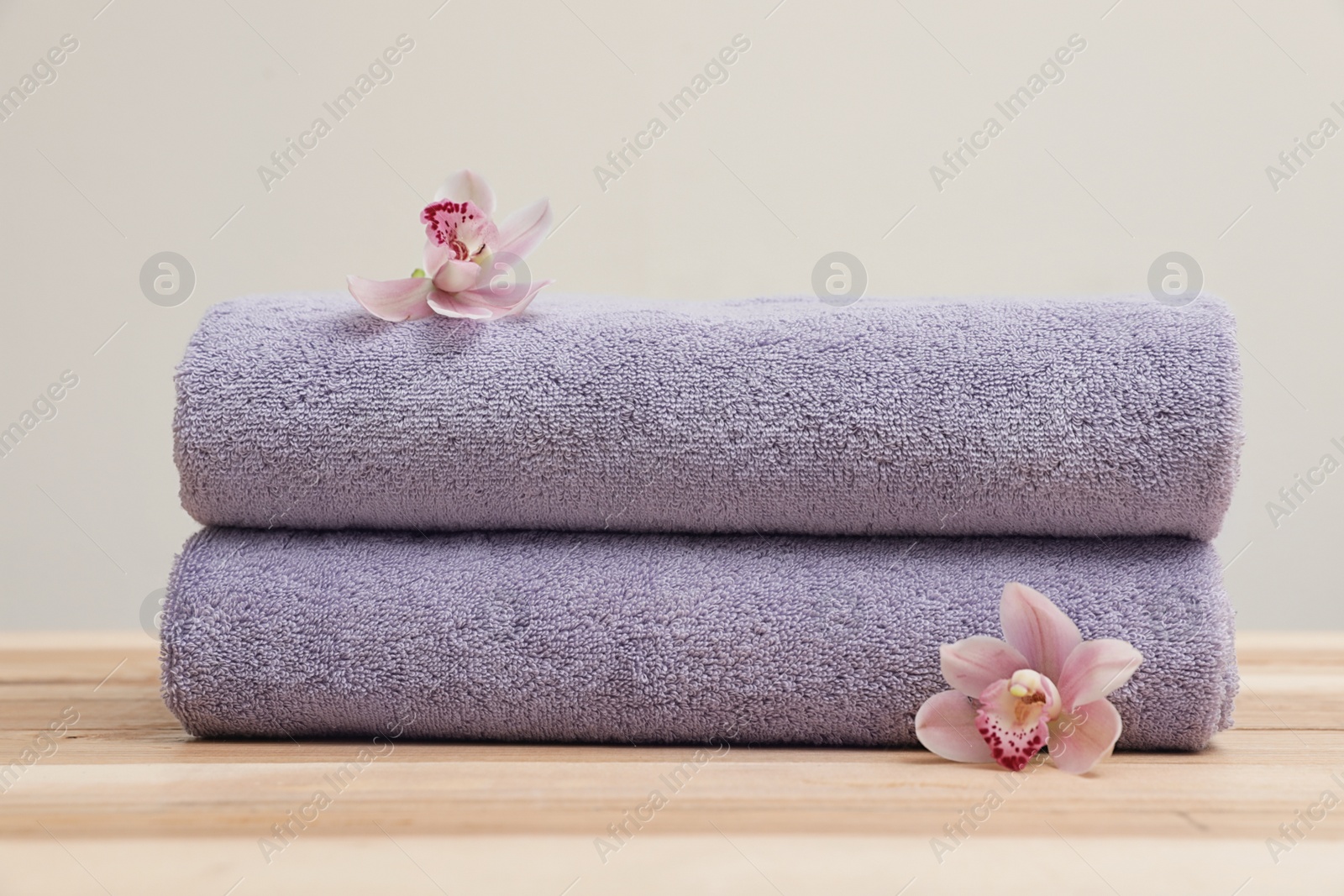 Photo of Stack of fresh towels with flowers on table