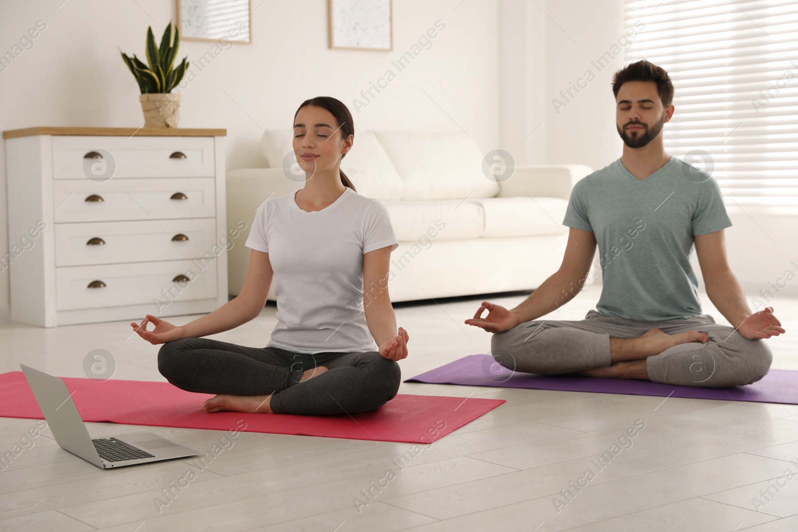 Photo of Couple practicing yoga while watching online class at home during coronavirus pandemic. Social distancing