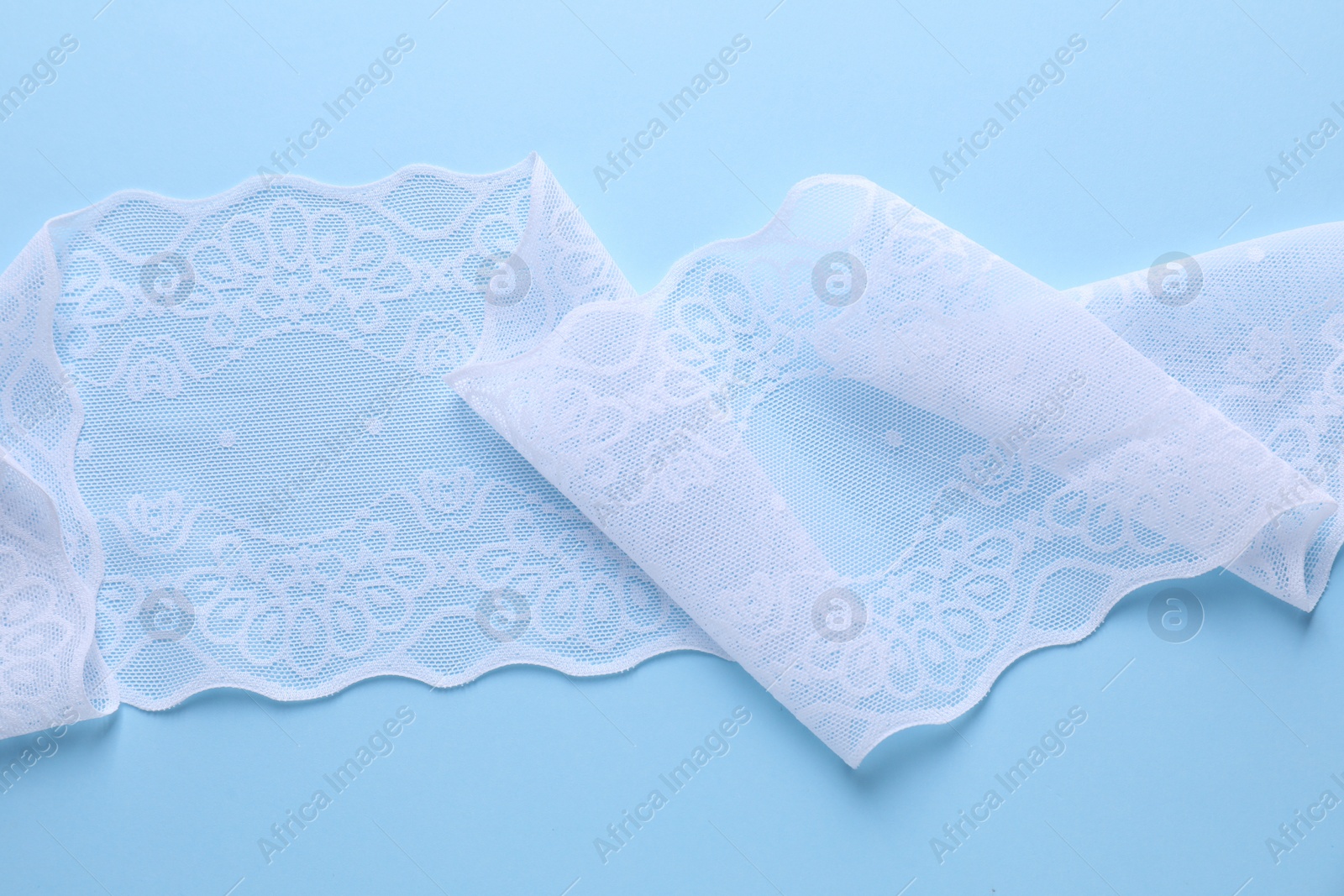 Photo of White lace on light blue background, top view