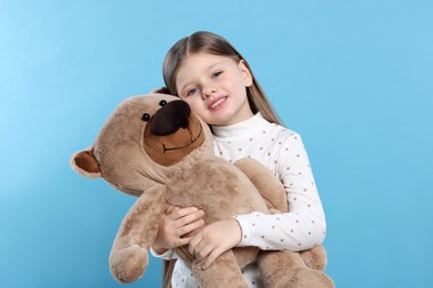 Photo of Cute little girl with teddy bear on light blue background