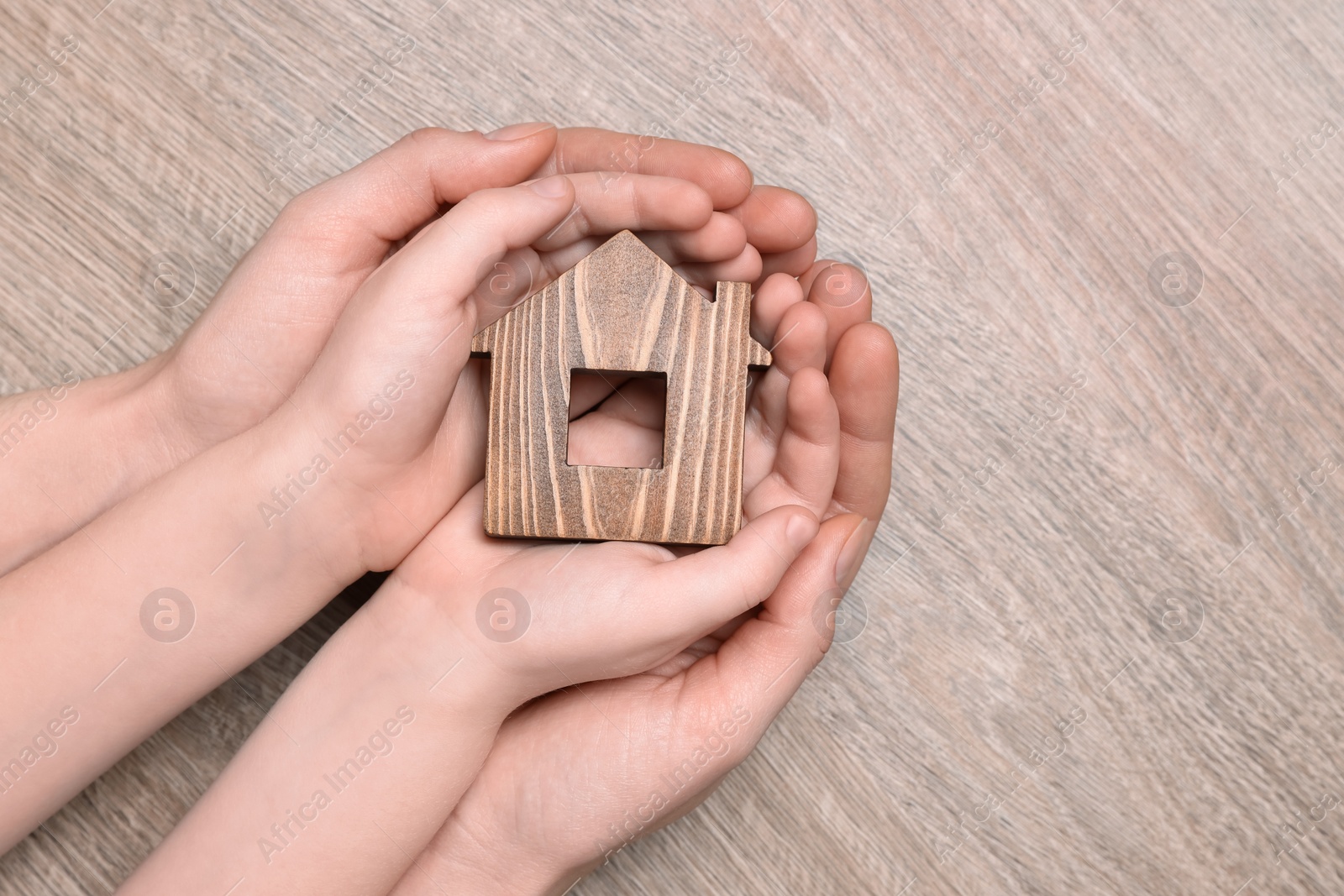 Photo of Home security concept. Woman and her little child holding house model at wooden table, top view with space for text