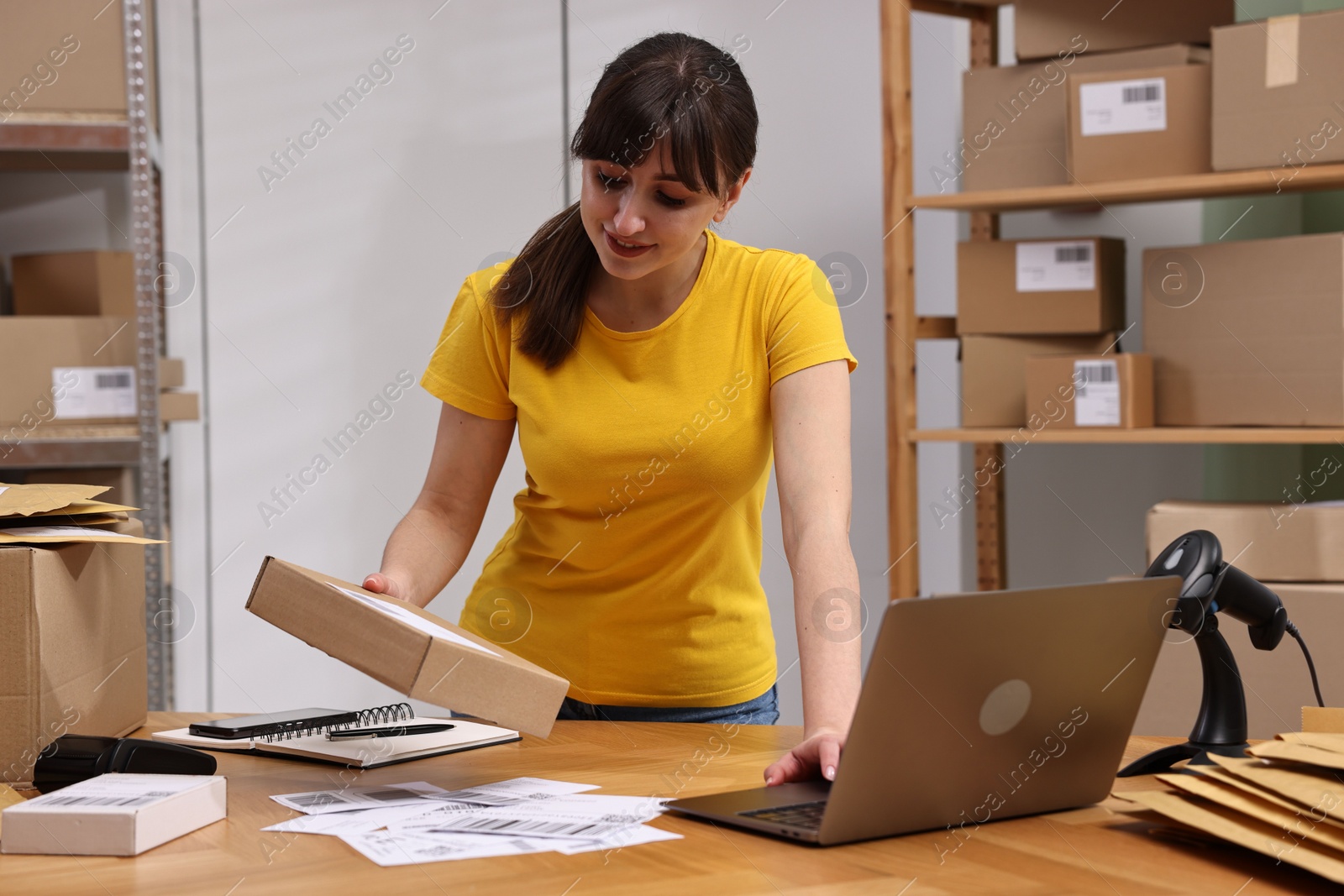 Photo of Parcel packing. Post office worker with box using laptop at wooden table indoors