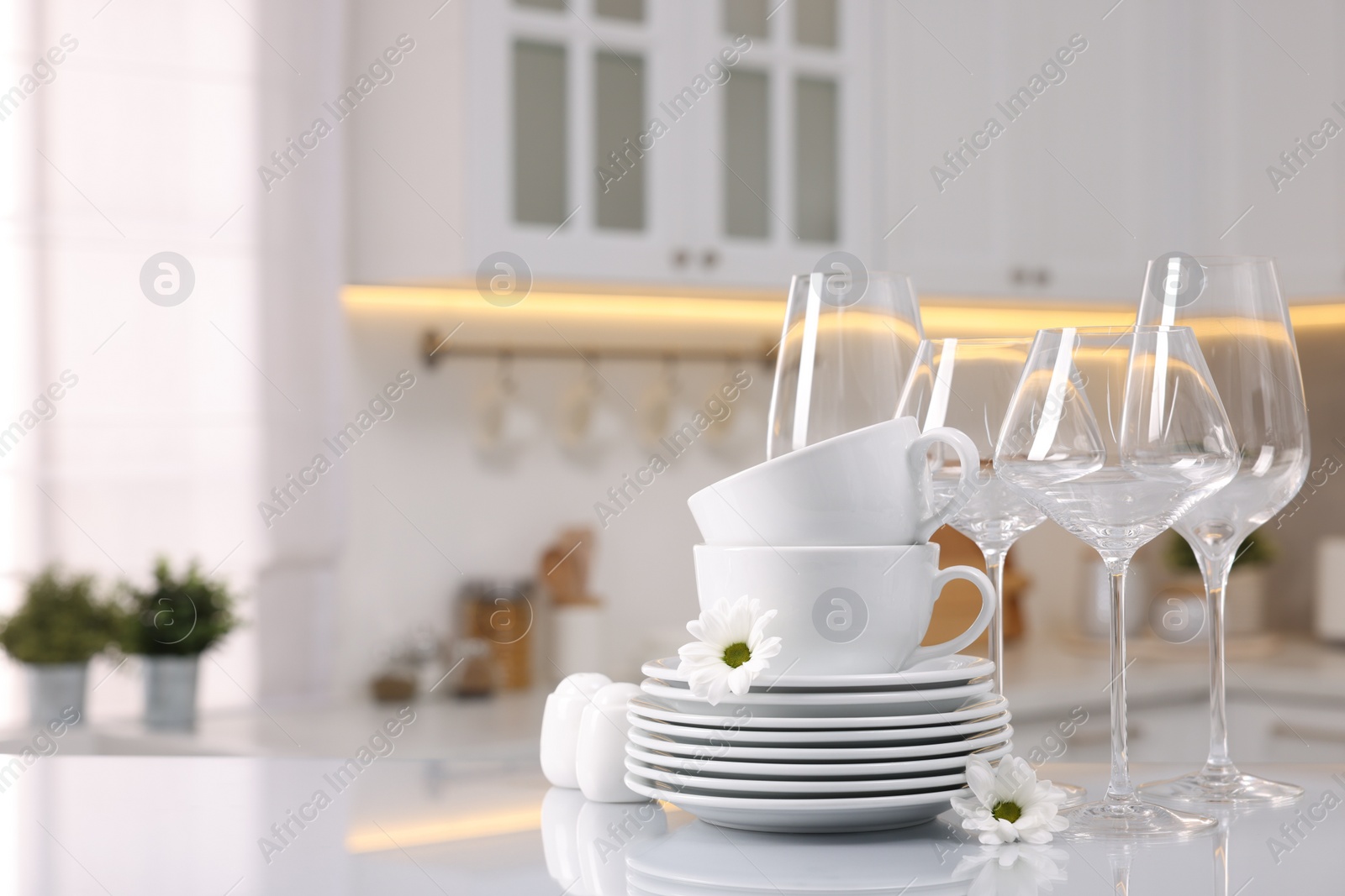 Photo of Set of clean dishware, glasses and flowers on table in kitchen, space for text