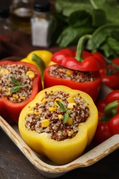 Photo of Quinoa stuffed bell peppers and basil in baking dish on wooden table, closeup