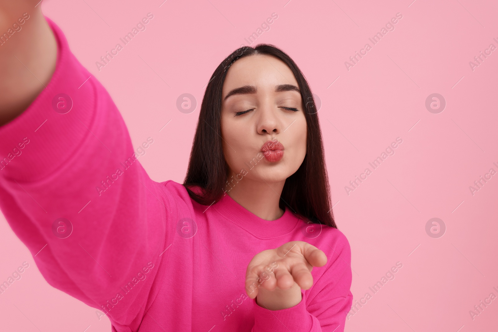 Photo of Young woman taking selfie and blowing kiss on pink background