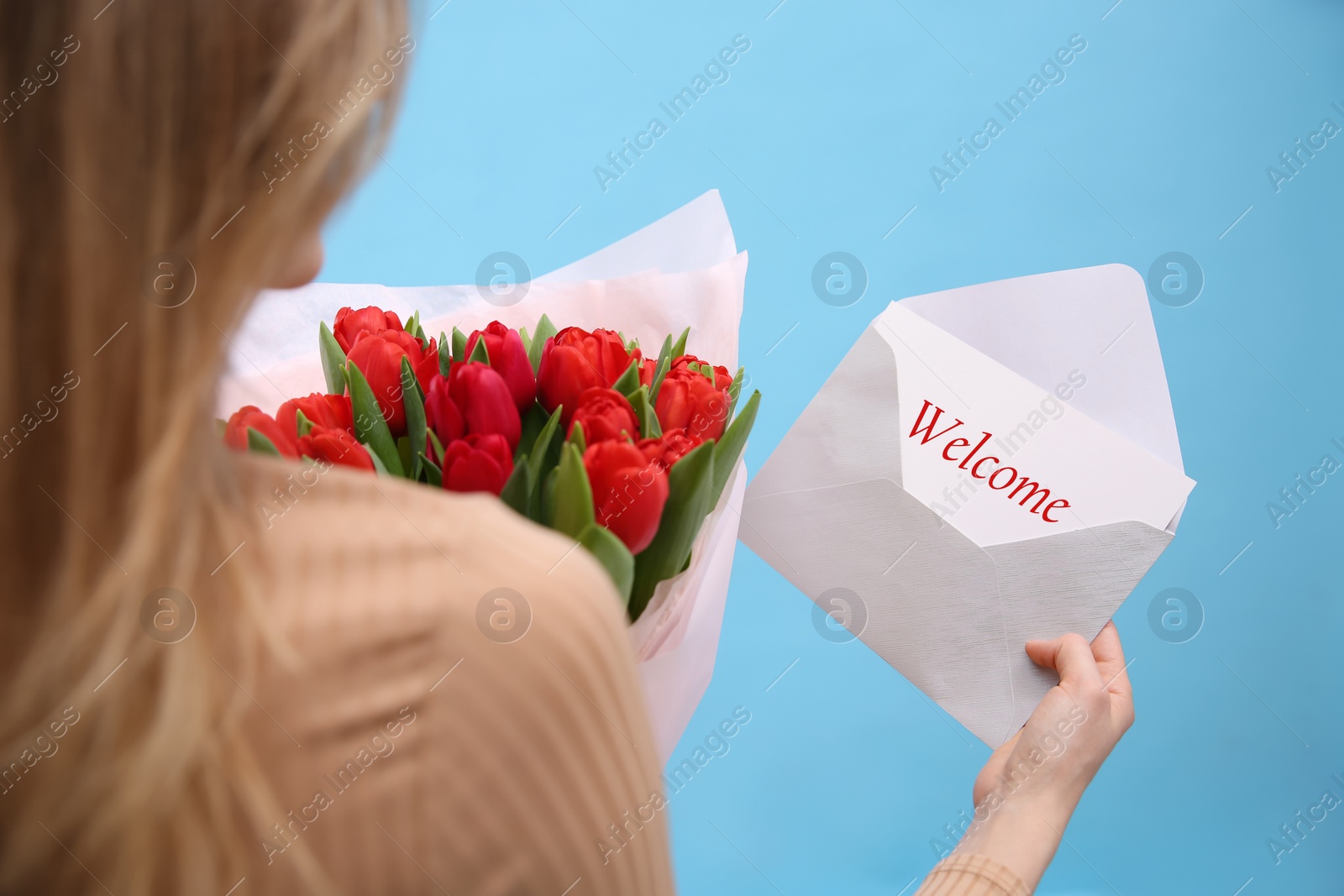 Image of Welcome card. Woman holding envelope and bouquet of red tulips on light blue background, closeup