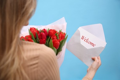 Welcome card. Woman holding envelope and bouquet of red tulips on light blue background, closeup