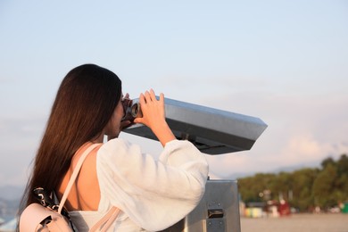 Photo of Young woman looking through tourist viewing machine at observation deck