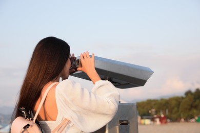 Young woman looking through tourist viewing machine at observation deck