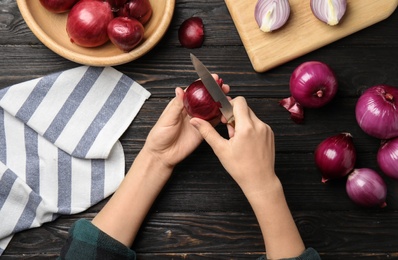 Photo of Woman peeling ripe red onion on wooden table, top view