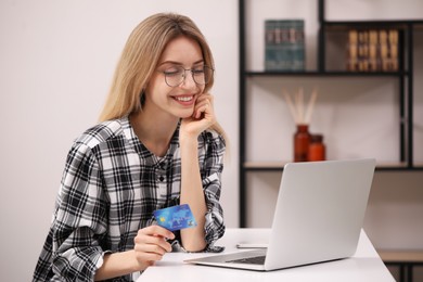 Photo of Woman with credit card using laptop for online shopping at white table indoors