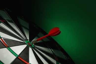 Photo of Red arrow hitting target on dart board against green background. Space for text