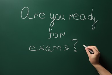 Photo of Woman writing phrase Are You Ready For Exams on green chalkboard, closeup