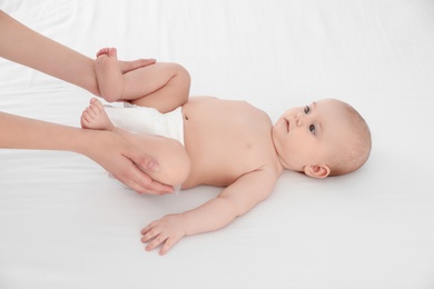 Photo of Mother and her cute child on white bed. Baby massage and exercises