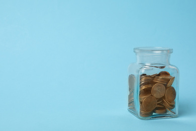 Glass jar with coins on light blue background, space for text