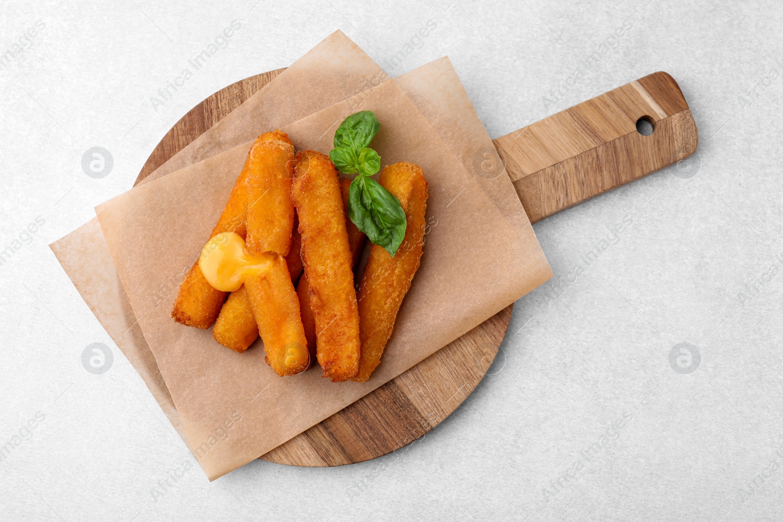 Photo of Tasty fried mozzarella sticks and basil on light table, top view