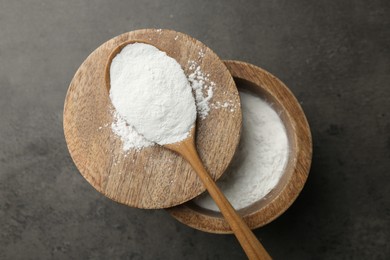 Photo of Baking powder in bowl and spoon on grey textured table, top view