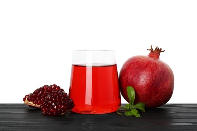 Photo of Refreshing pomegranate juice in glass, leaves and fruits on black wooden table against white background