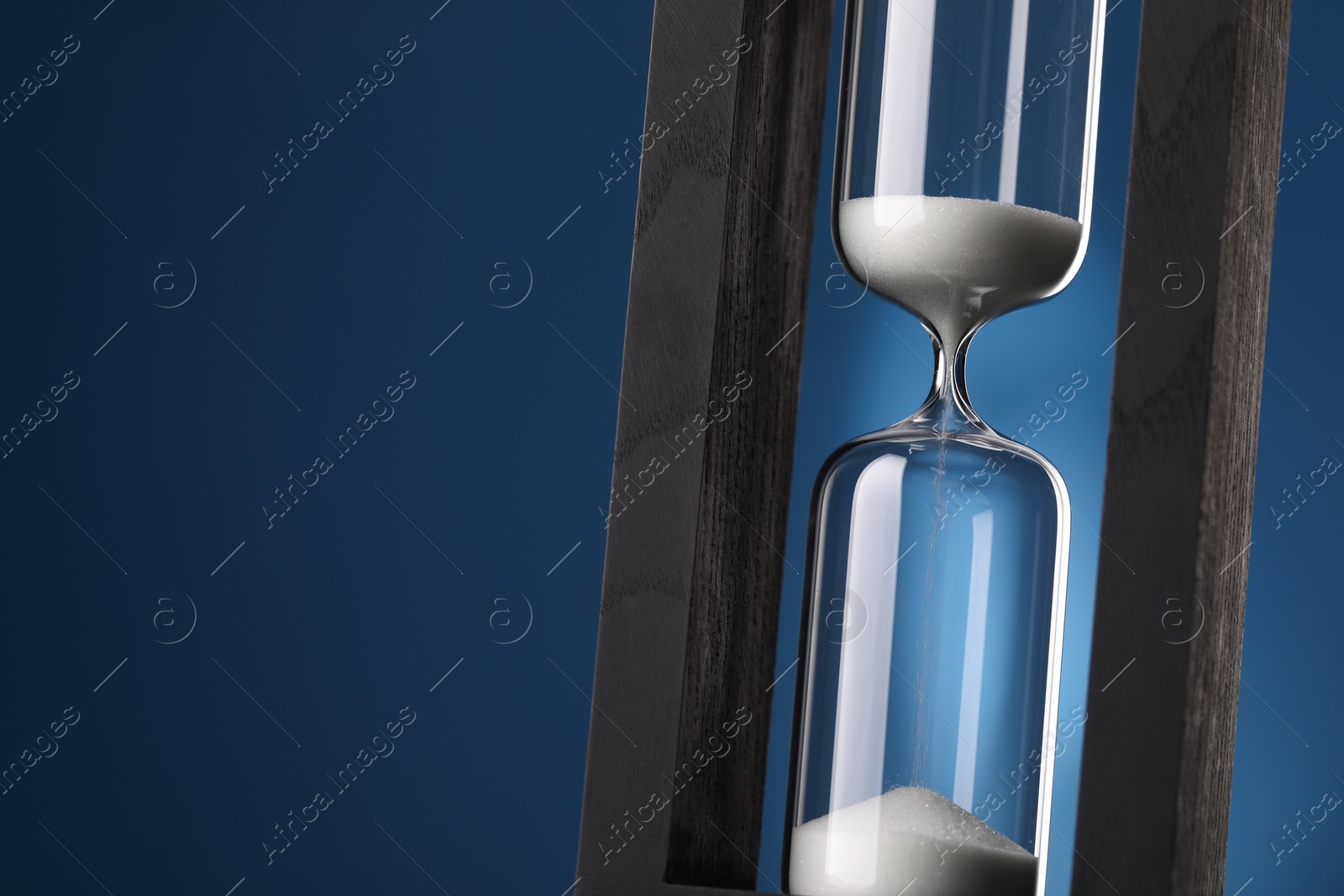 Photo of Hourglass with flowing sand on blue background, closeup. Space for text