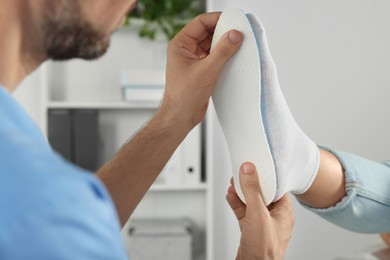 Photo of Male orthopedist fitting insole to patient's foot in hospital, closeup