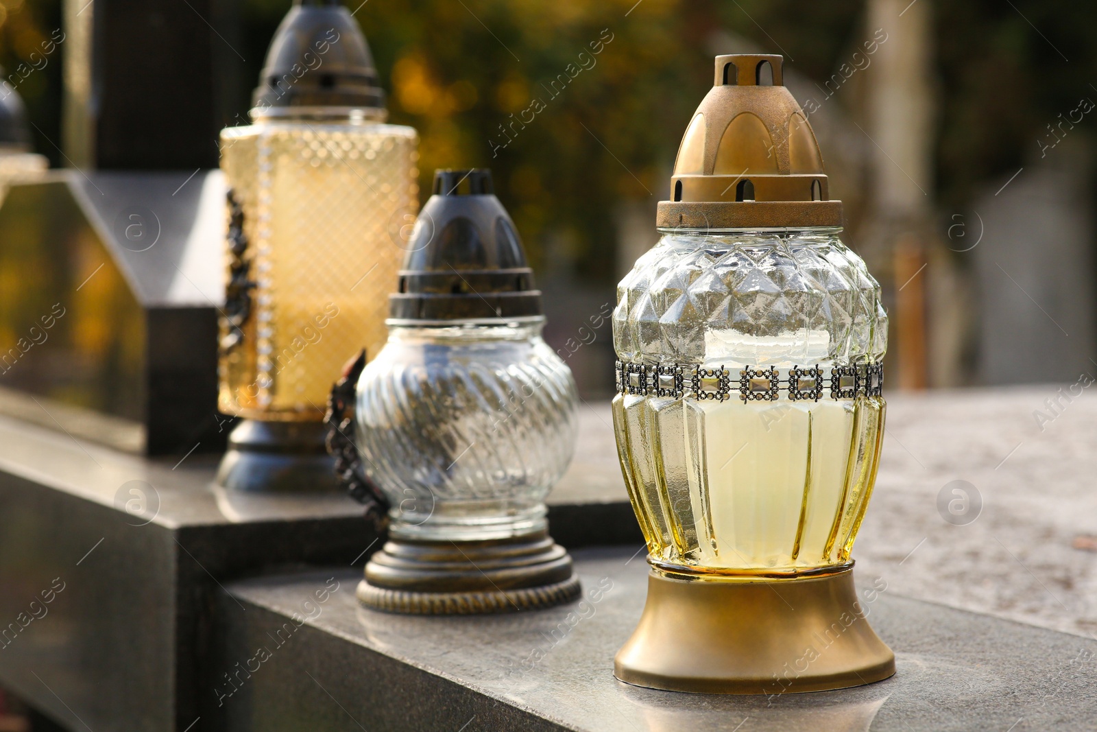 Photo of Different grave lanterns on granite tombstone outdoors, space for text. Funeral ceremony