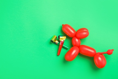 Party blowers and dog figure made of modelling balloon on green background, flat lay. Space for text