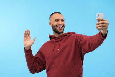 Photo of Smiling young man taking selfie with smartphone on light blue background