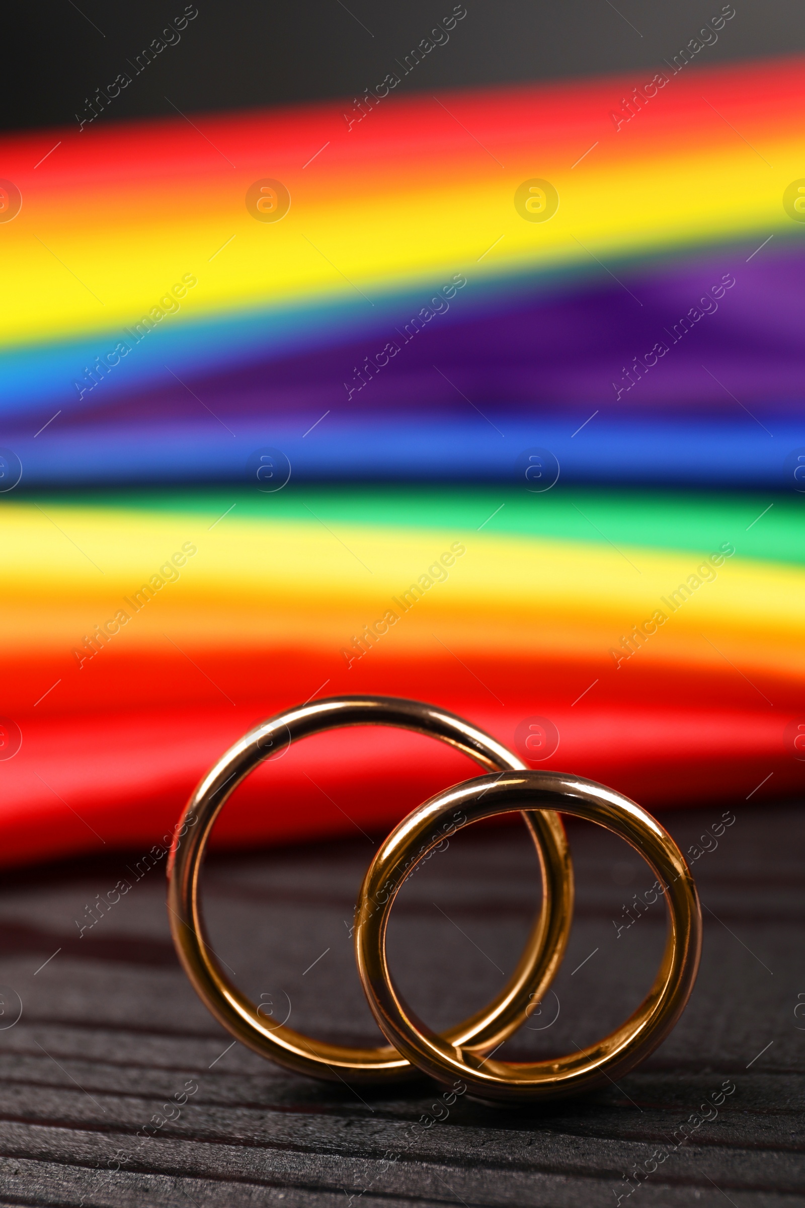 Photo of Rainbow LGBT flag and wedding rings on black wooden background, closeup