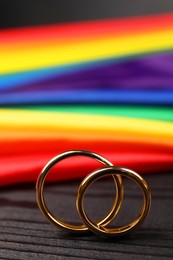 Rainbow LGBT flag and wedding rings on black wooden background, closeup
