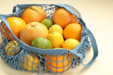 Photo of String bag with different fruits on beige background, closeup