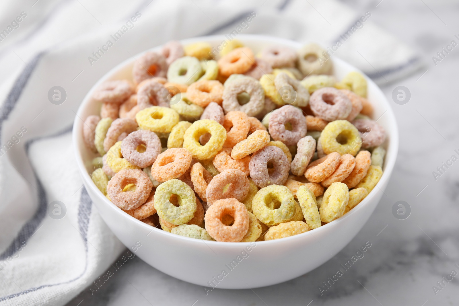 Photo of Tasty cereal rings in bowl on white marble table, closeup