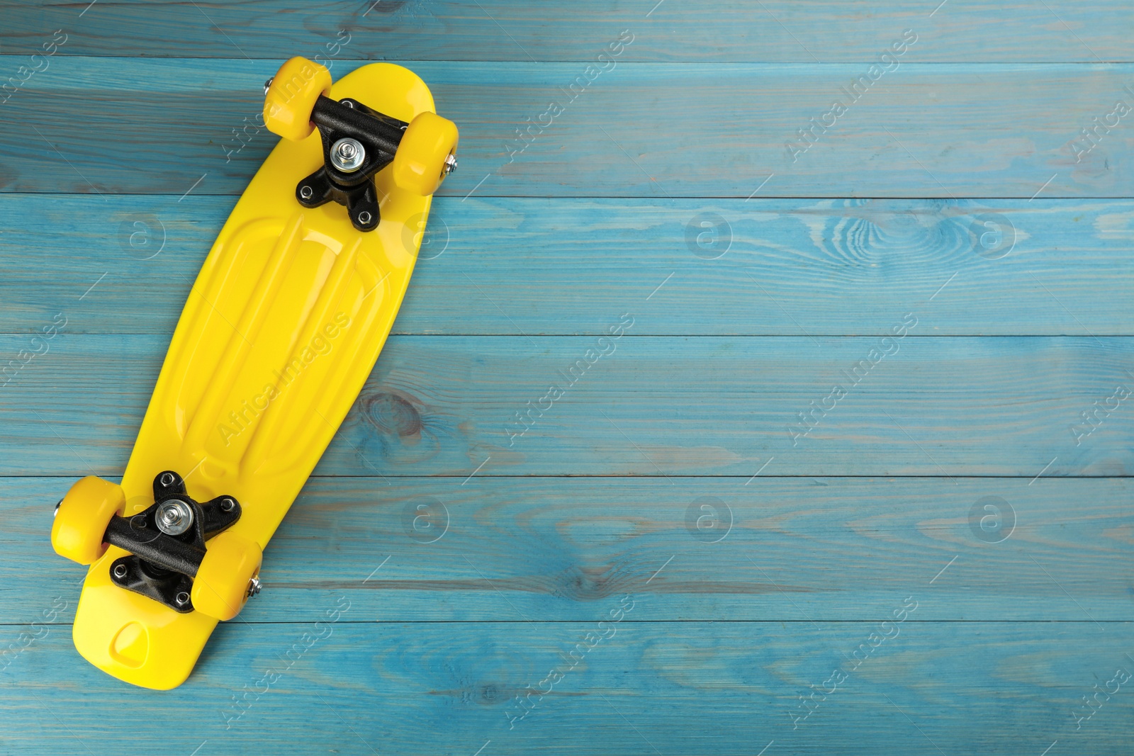 Photo of Yellow skateboard on turquoise wooden background, top view. Space for text